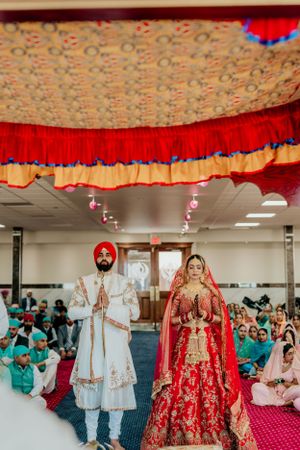 Sikh wedding ceremony under decorative canopy with couple in traditional white and red attire.