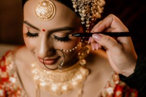 Close-up shot of traditional Indian bridal makeup application with gold jewelry.