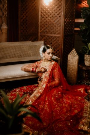 Traditional red bridal lehenga photographed in elegant indoor setting with wooden decor.