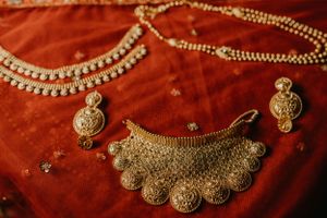 Ornate gold Indian wedding jewelry and necklaces displayed on red fabric.