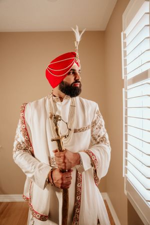 Traditional Sikh wedding attire featuring an ornate white sherwani and red turban with decorative elements.