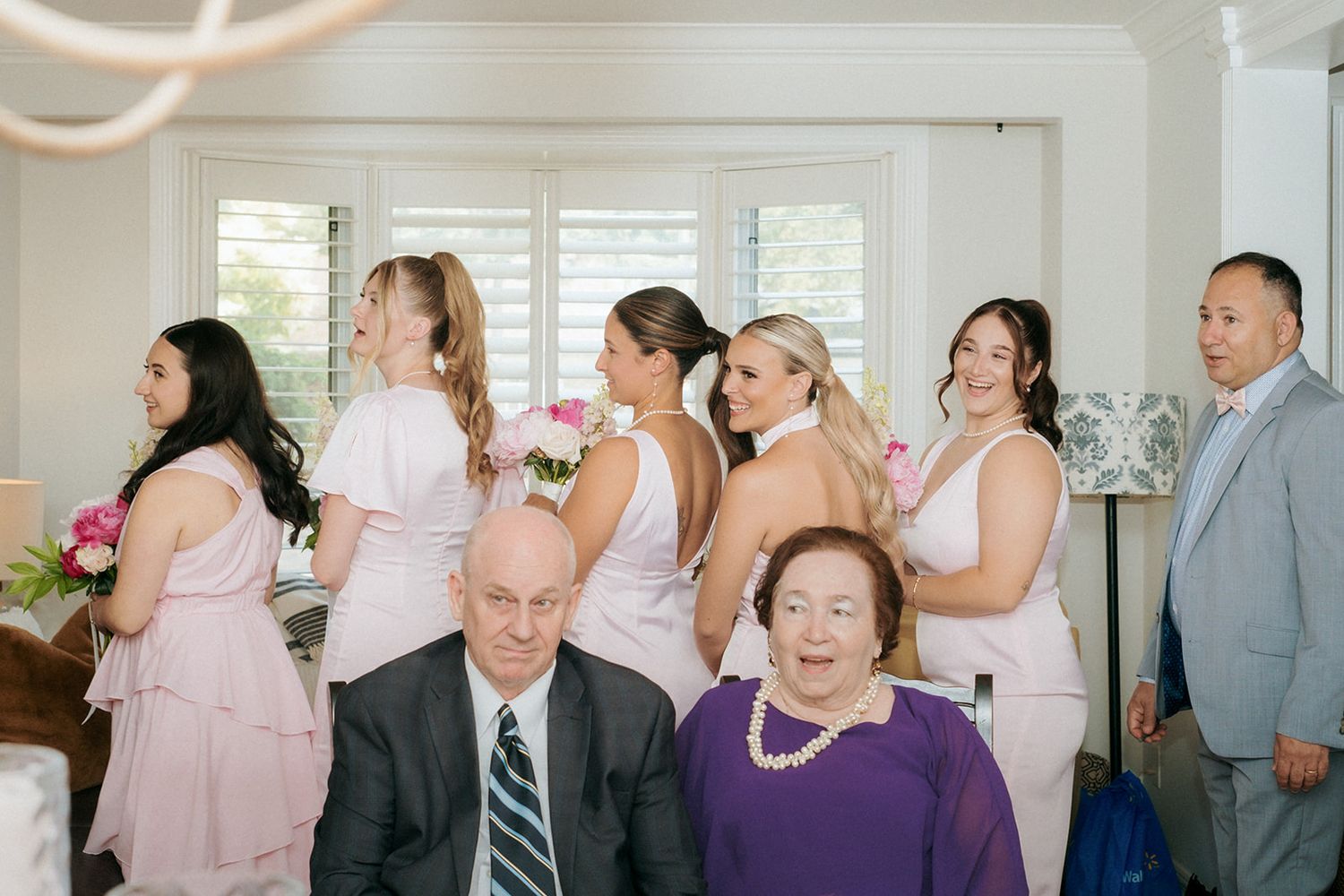 Wedding party gathering in bright indoor space with pink and gray attire.