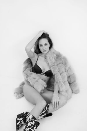 Black and white fashion photo featuring a model in lingerie and fur coat posing against white background.