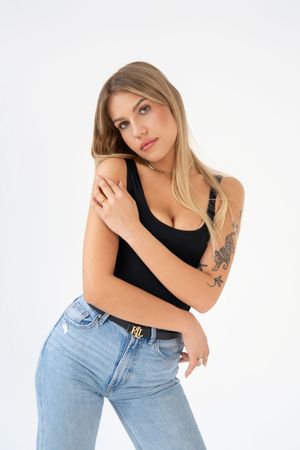Woman in black tank top and light jeans poses against white background in casual fashion style.