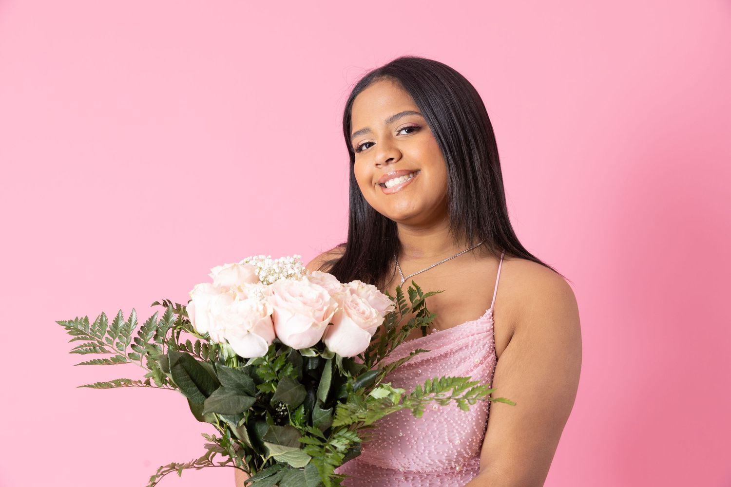 Woman in pink dress holds bouquet of light pink roses against a pink background.