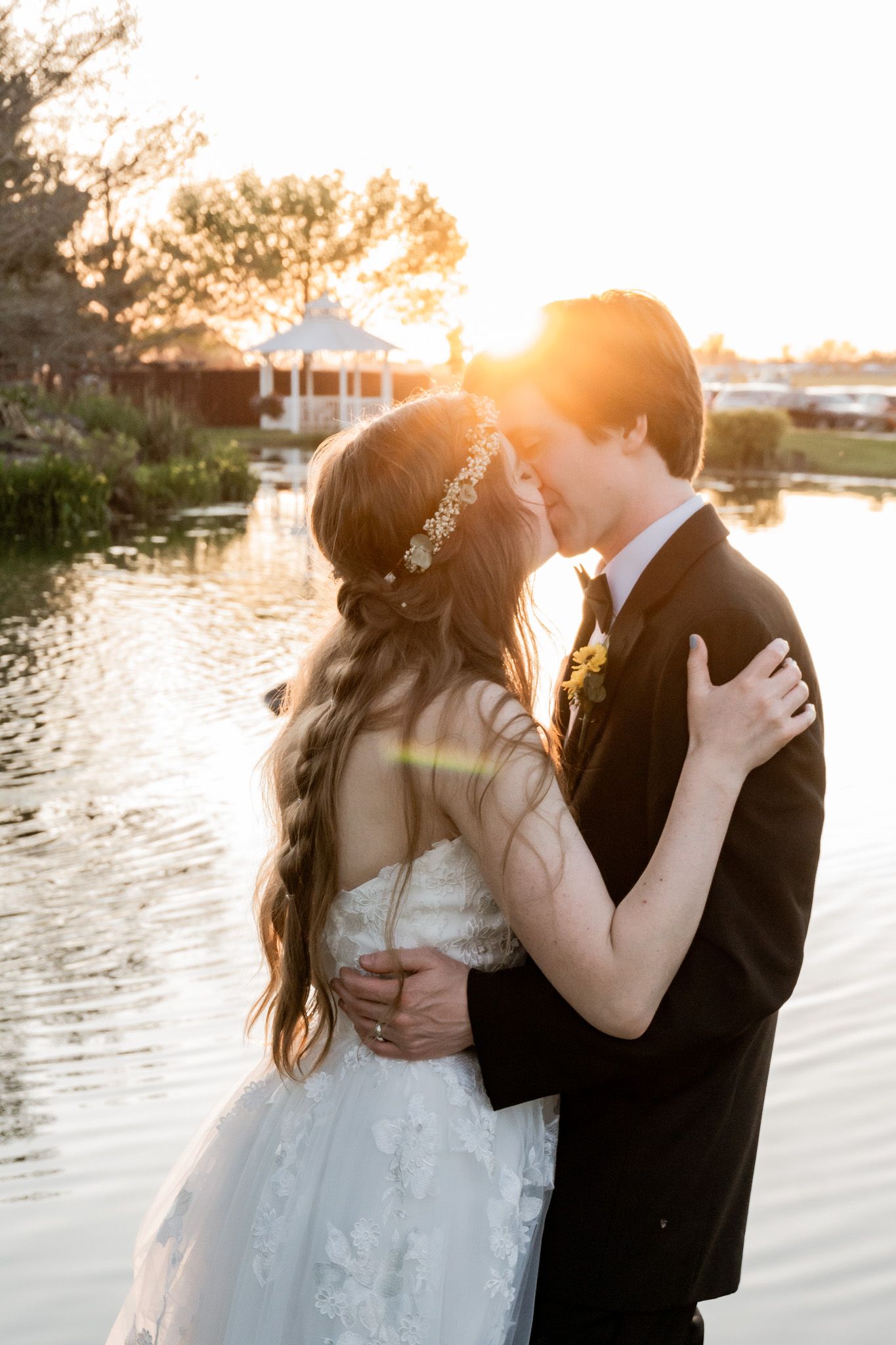 A romantic sunset wedding portrait by a lake with golden light filtering through the trees.