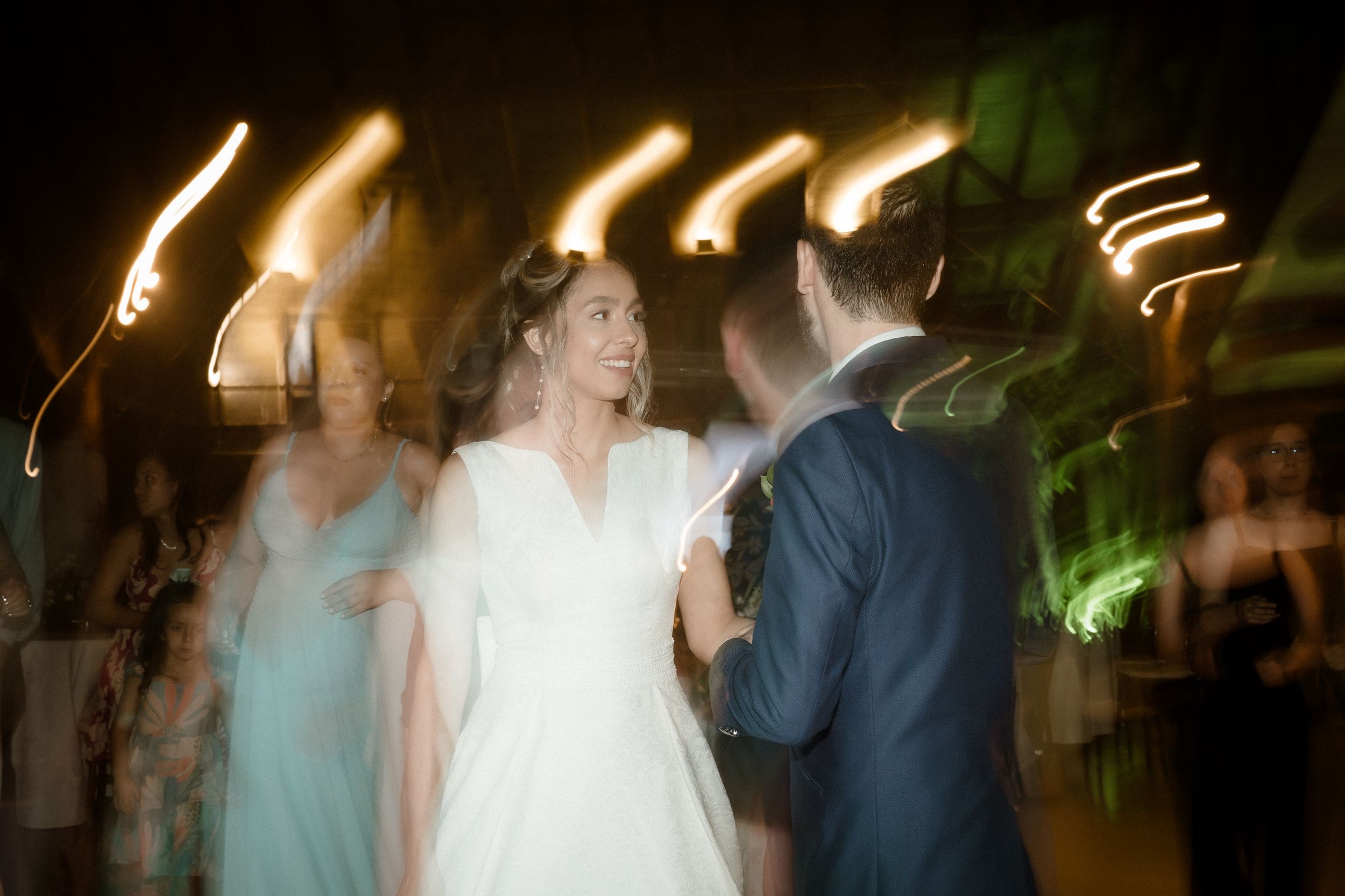 Blurred motion shot of wedding dancers under ambient lighting creates dreamy atmosphere.