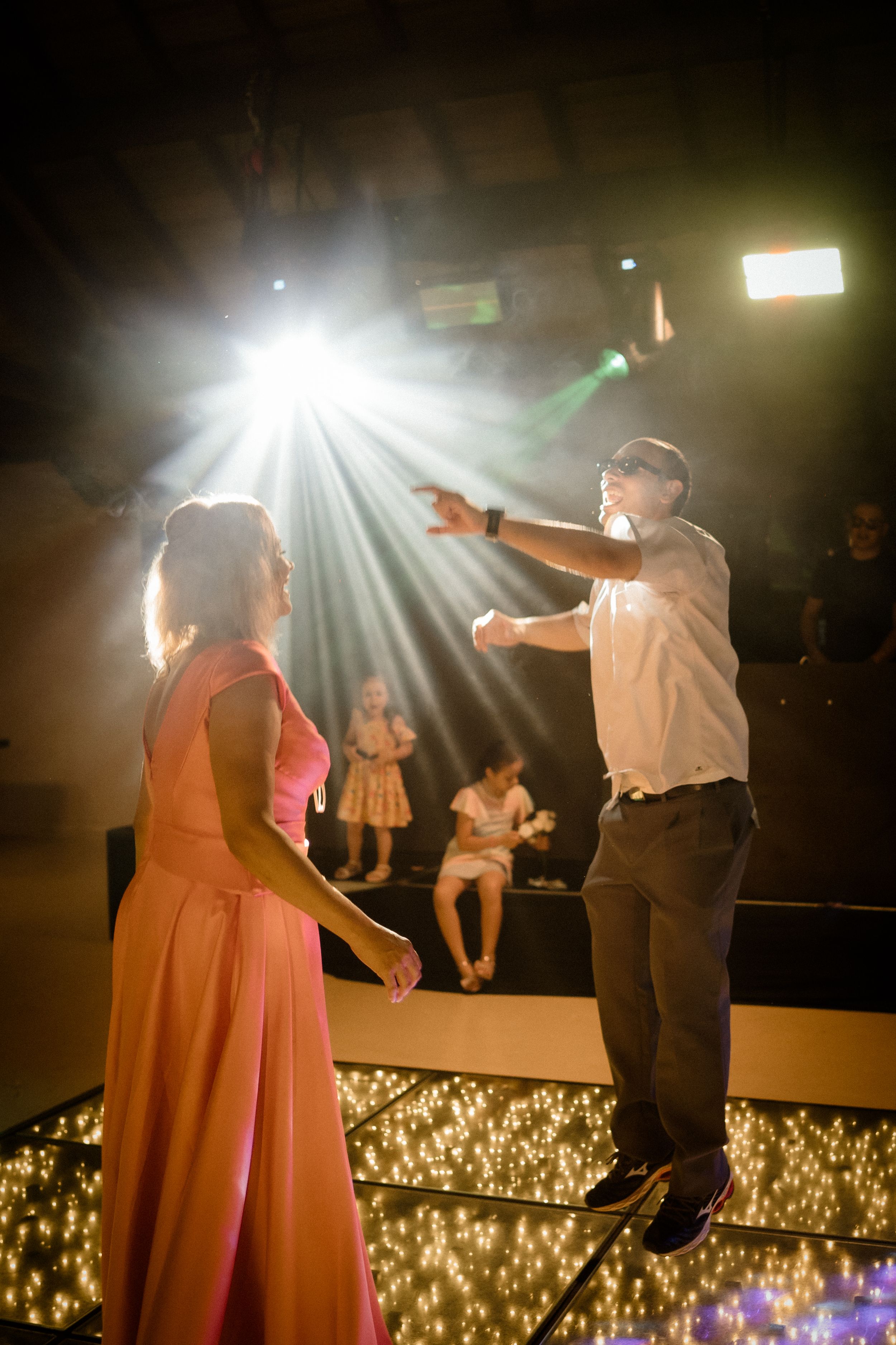 A couple dances energetically under dramatic spotlights on a stage decorated with twinkling lights below.