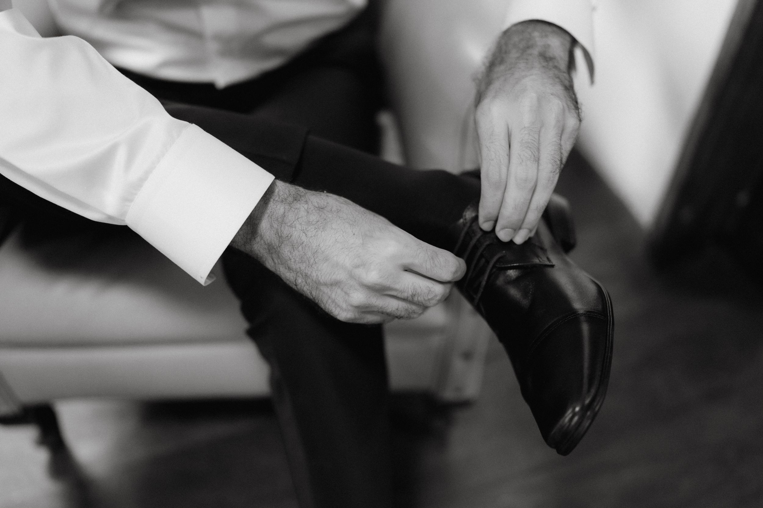 Close-up shot of hands adjusting formal dress shoes in black and white.