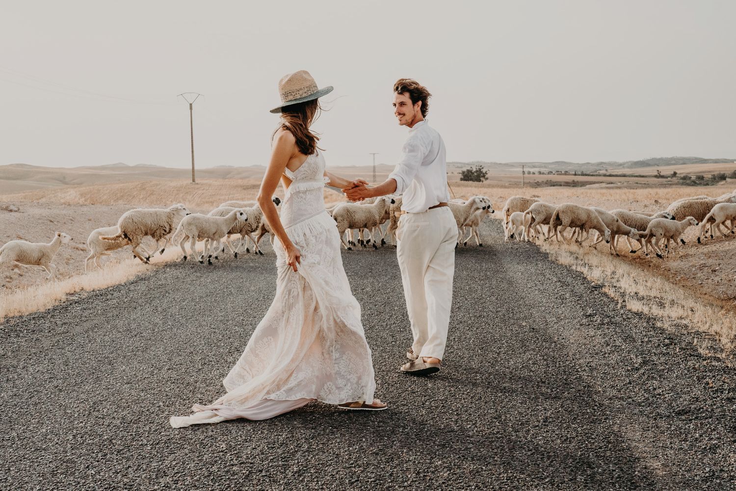 Couple dancing on rural road with sheep herd wandering in desert background.