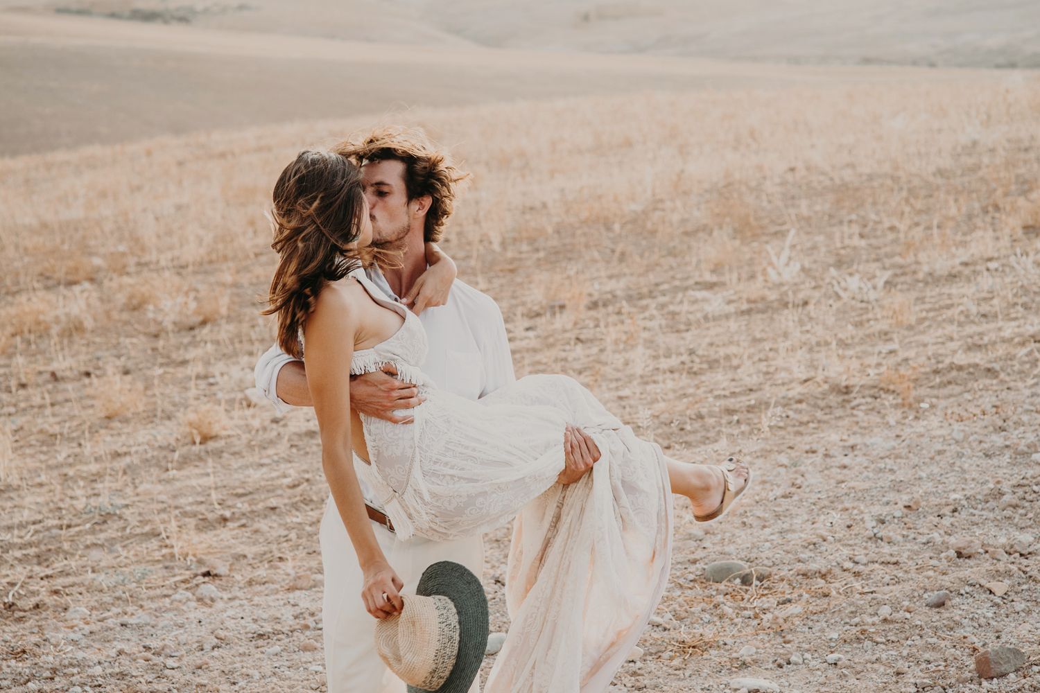 A romantic couple in white attire embraces in a dreamy golden field during sunset.