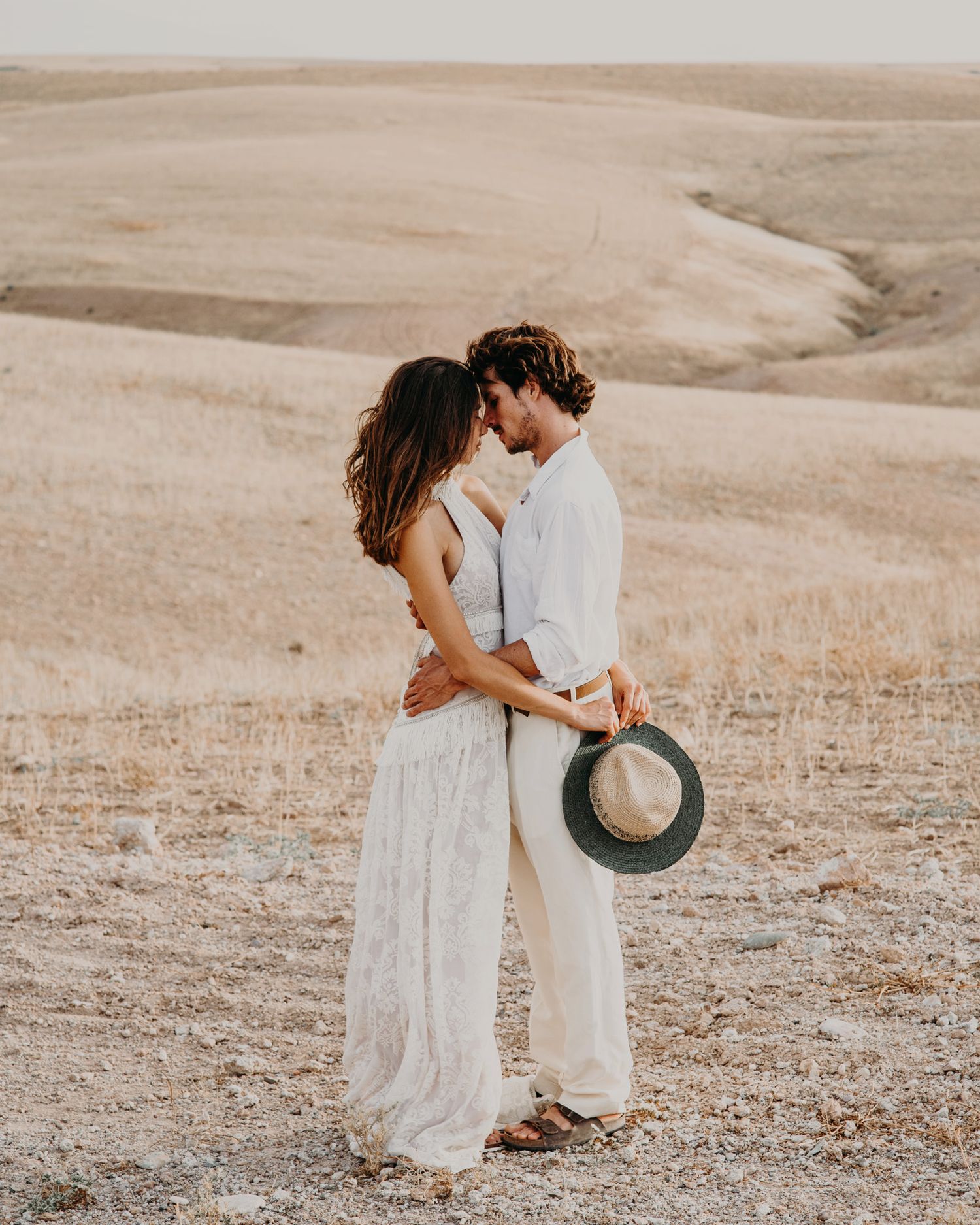 Couple in flowing white clothes share an intimate moment in a golden desert landscape.