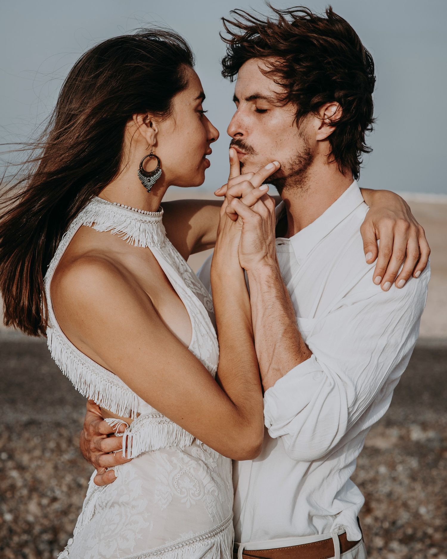 Passionate close-up of a couple in white outfits against a moody background.