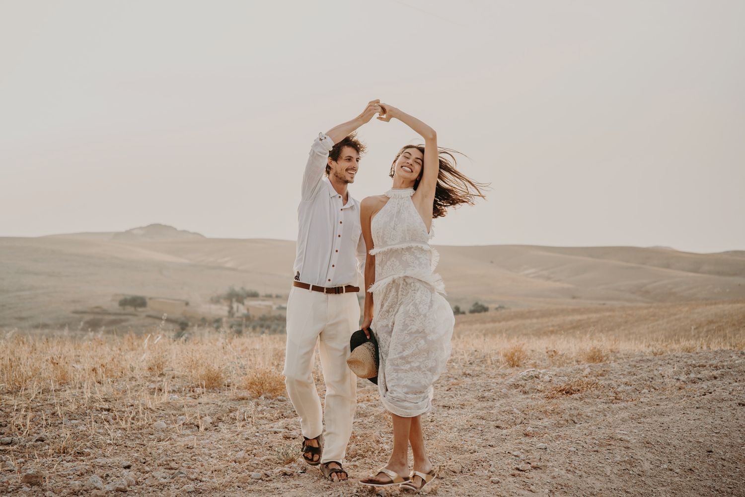 A couple creating a heart shape with their arms while dancing in a desert landscape.