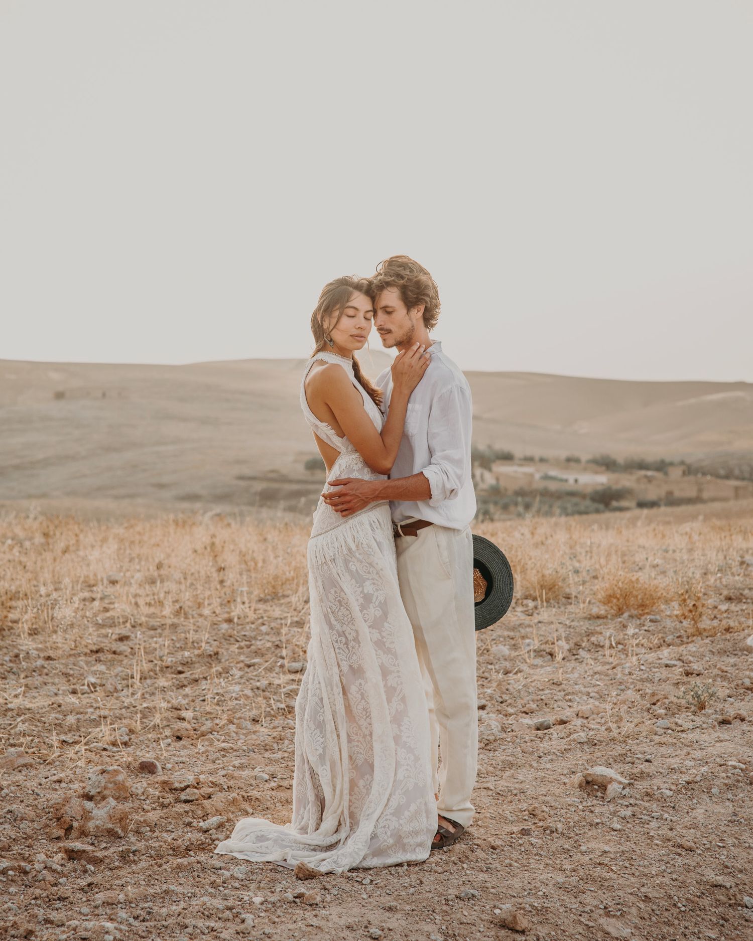 A tender embrace between a couple wearing white in a desert setting.