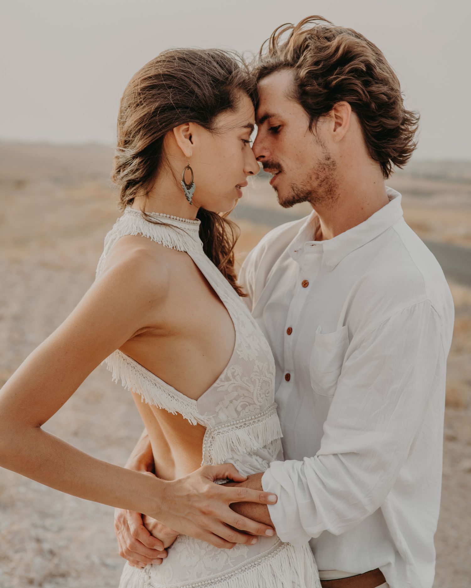 An intimate moment between a couple in white clothing against a desert backdrop.