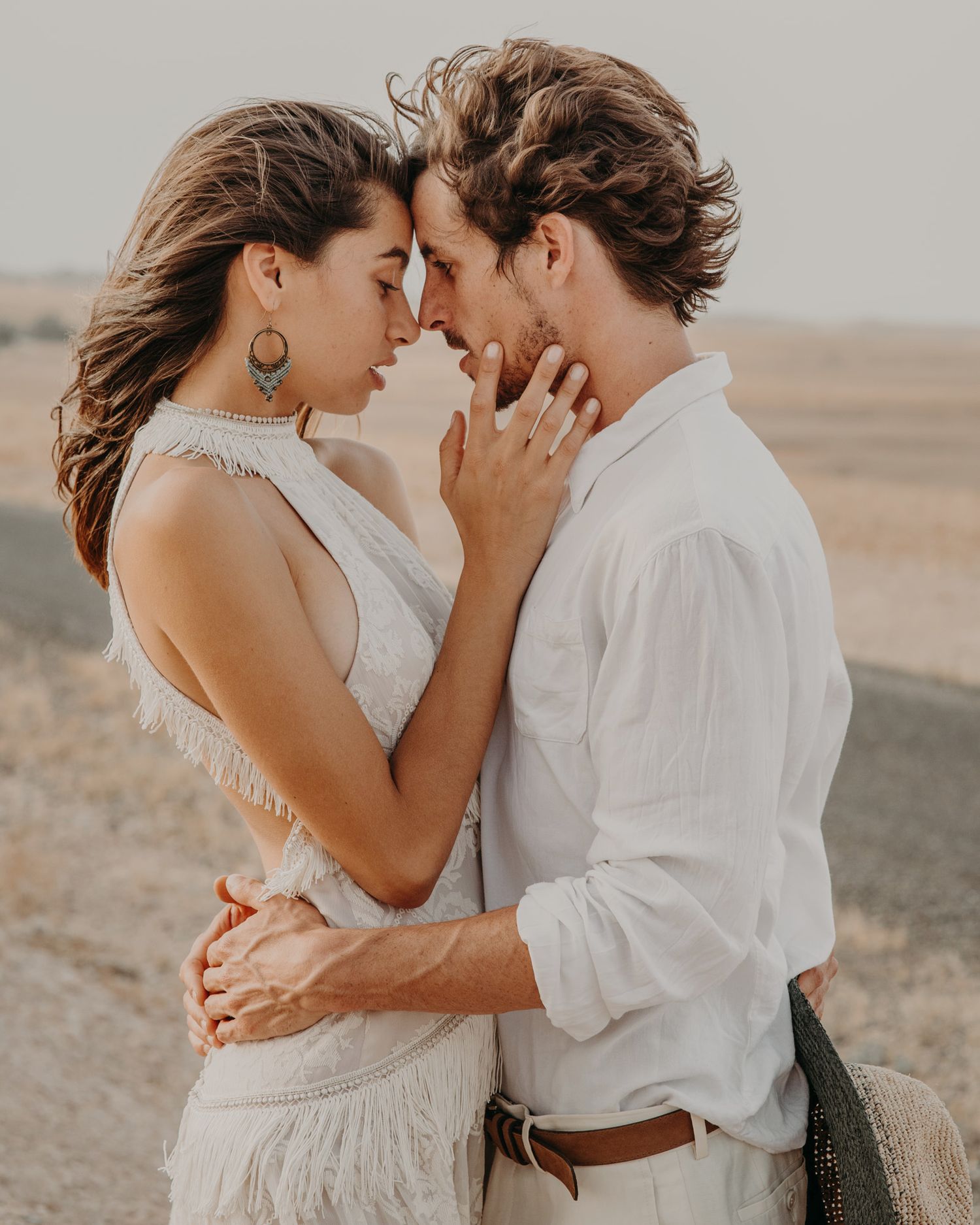 A tender moment between a couple in white clothing against a desert landscape.