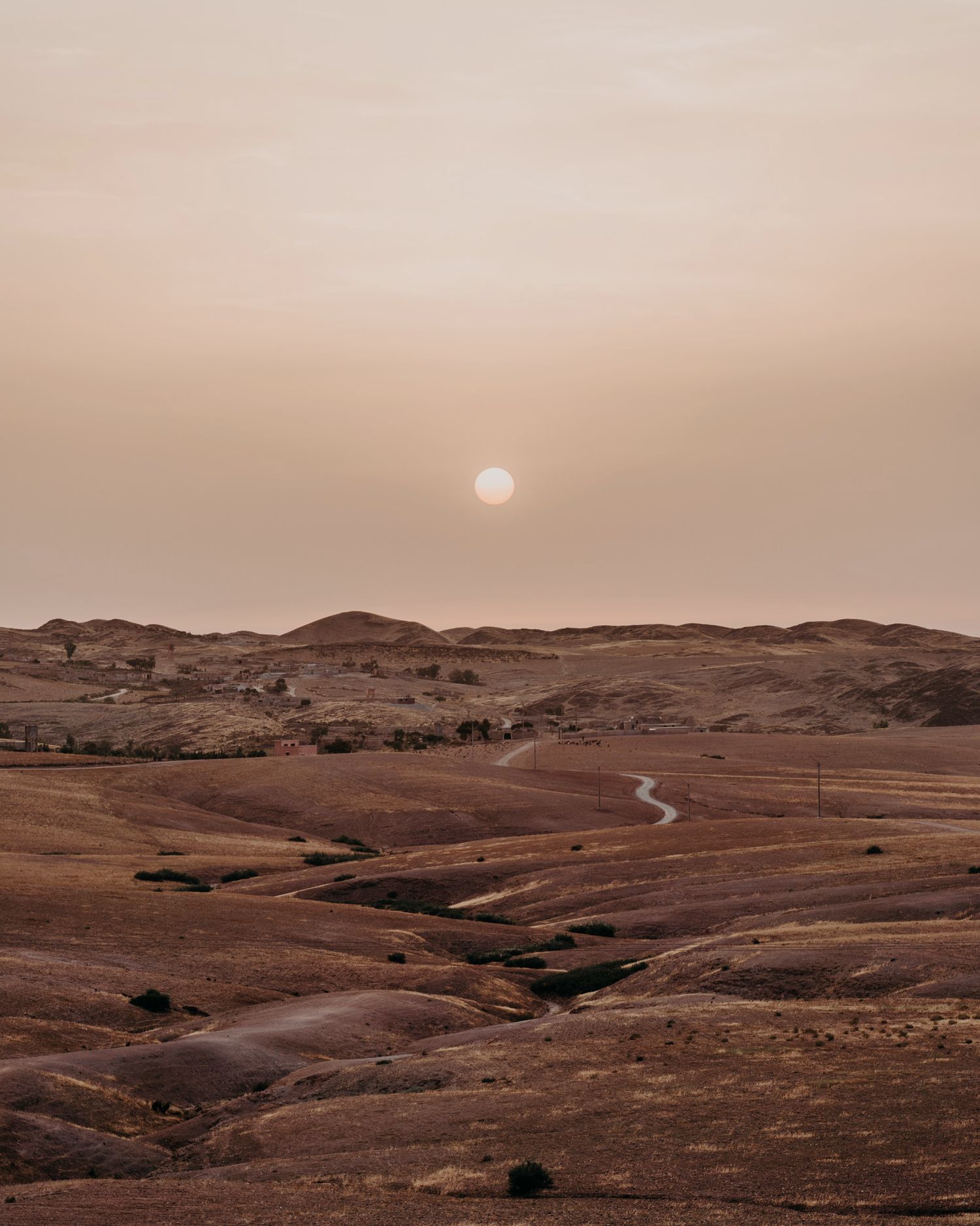 Sunset over rolling desert hills creates a warm, ethereal landscape view.