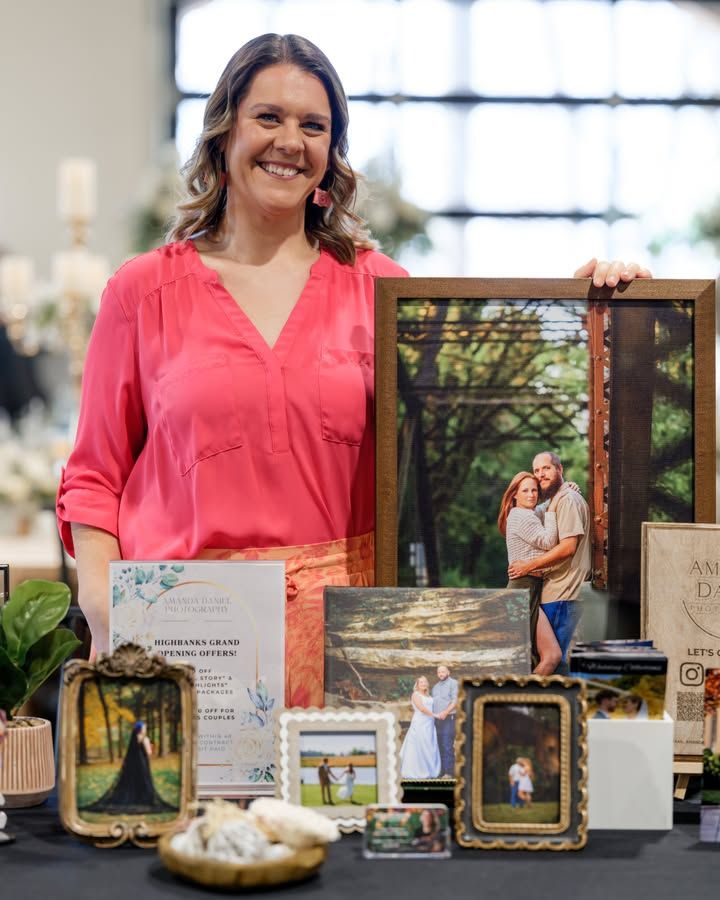 Professional photographer displays portfolio of wedding and engagement photos with framed prints on a black table.