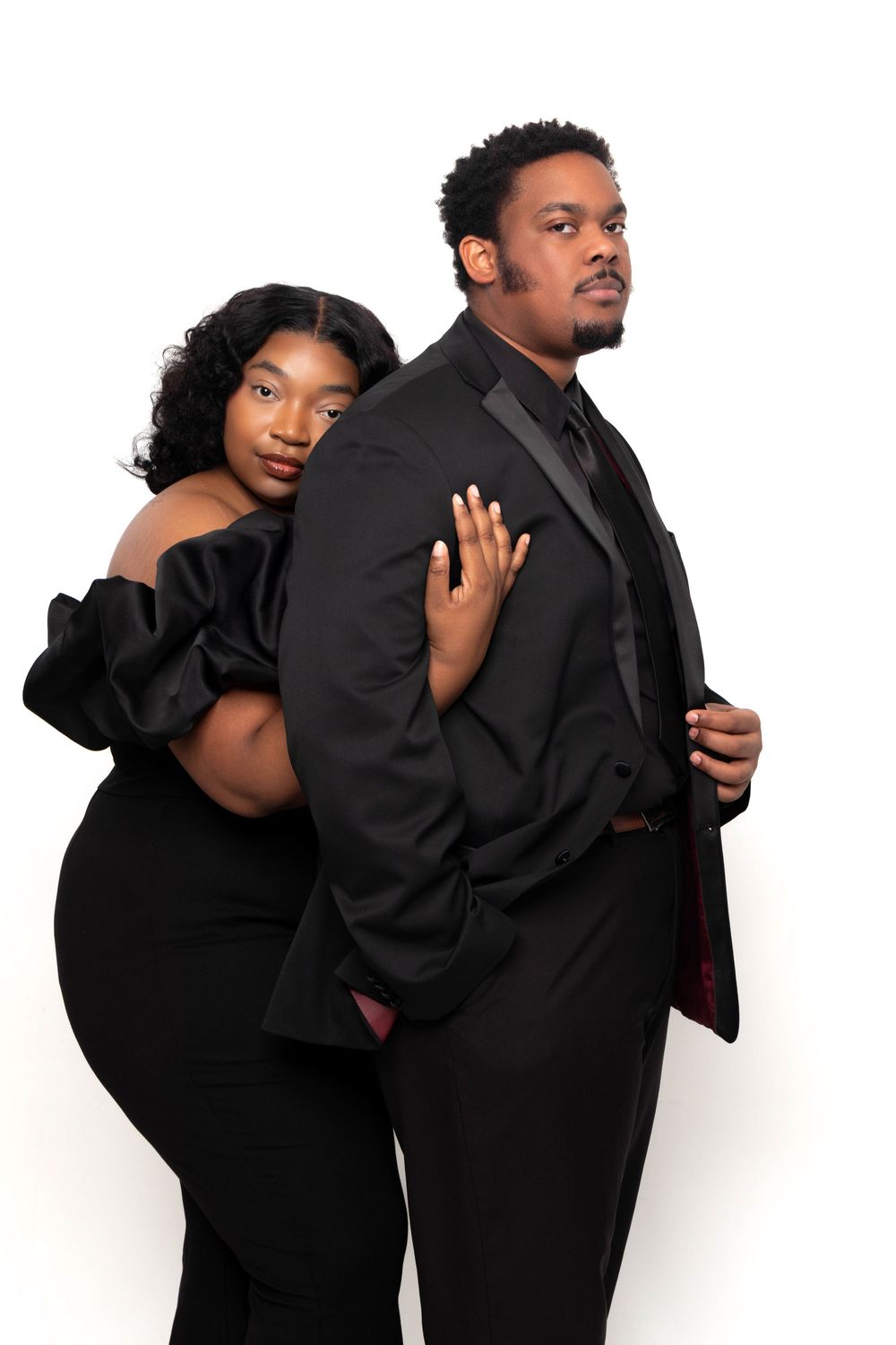 Elegant couple in matching black formal attire posing together against a white background.