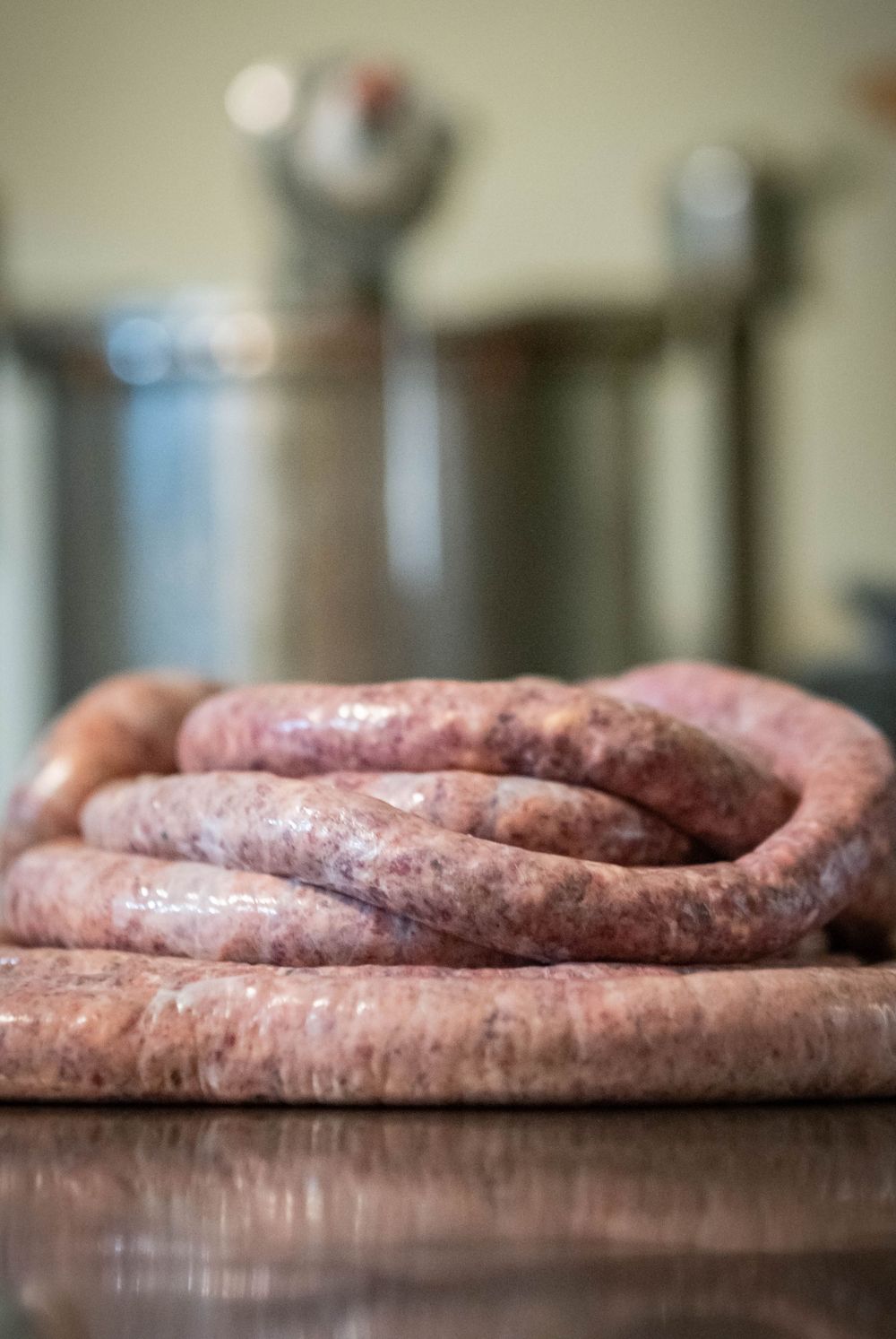 Fresh homemade sausage coiled on wooden cutting board in commercial kitchen.