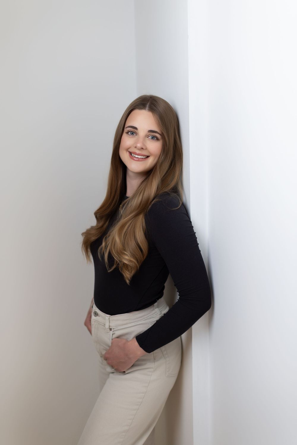 Professional studio portrait series showing a person in a black sweater and beige skirt posing against a white wall.