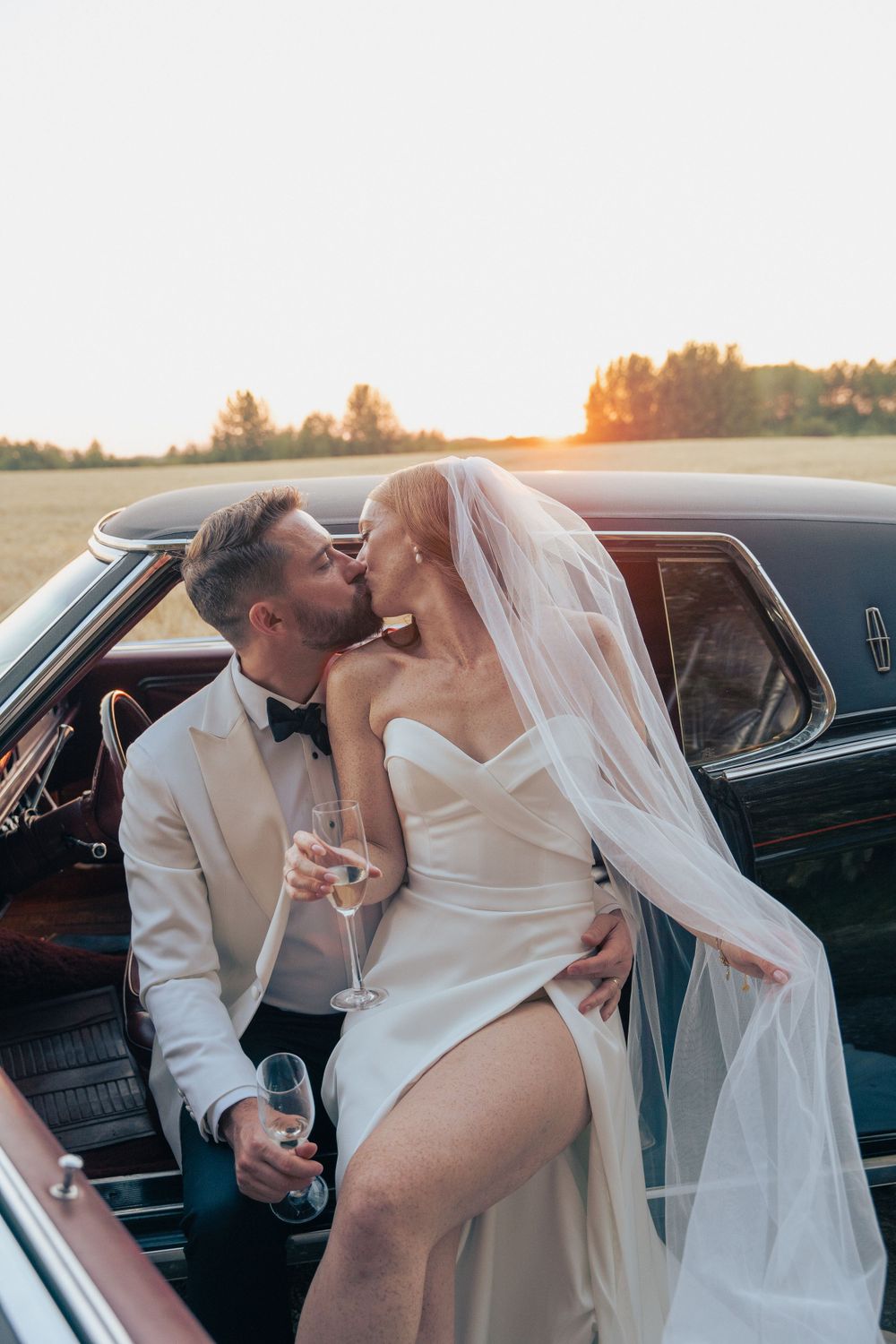 A romantic sunset moment by a vintage car during a wedding photoshoot.