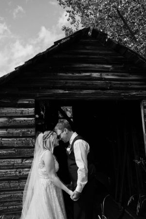 A rustic black and white wedding photo in front of a log cabin.