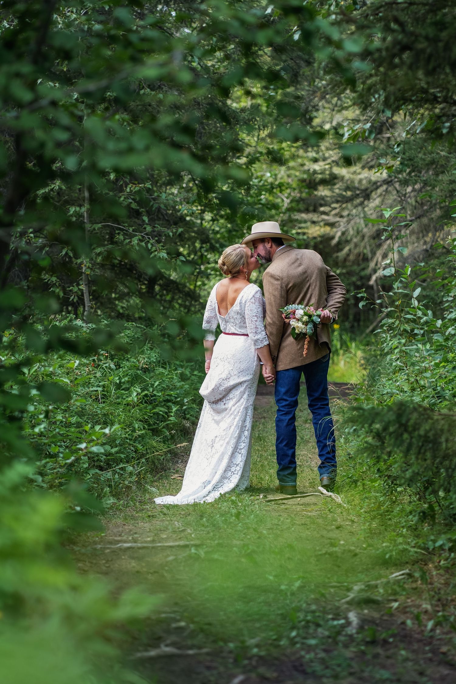 A romantic countryside wedding photo of a couple walking on a tree-lined path in nature.