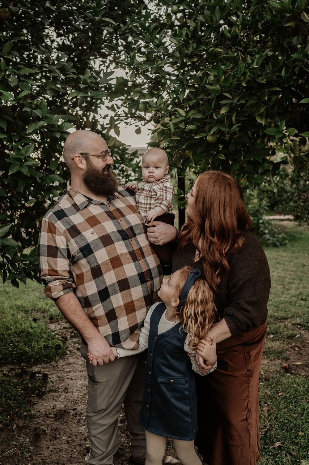A family of three shares tender moments together in an outdoor garden setting with lush greenery in the background.