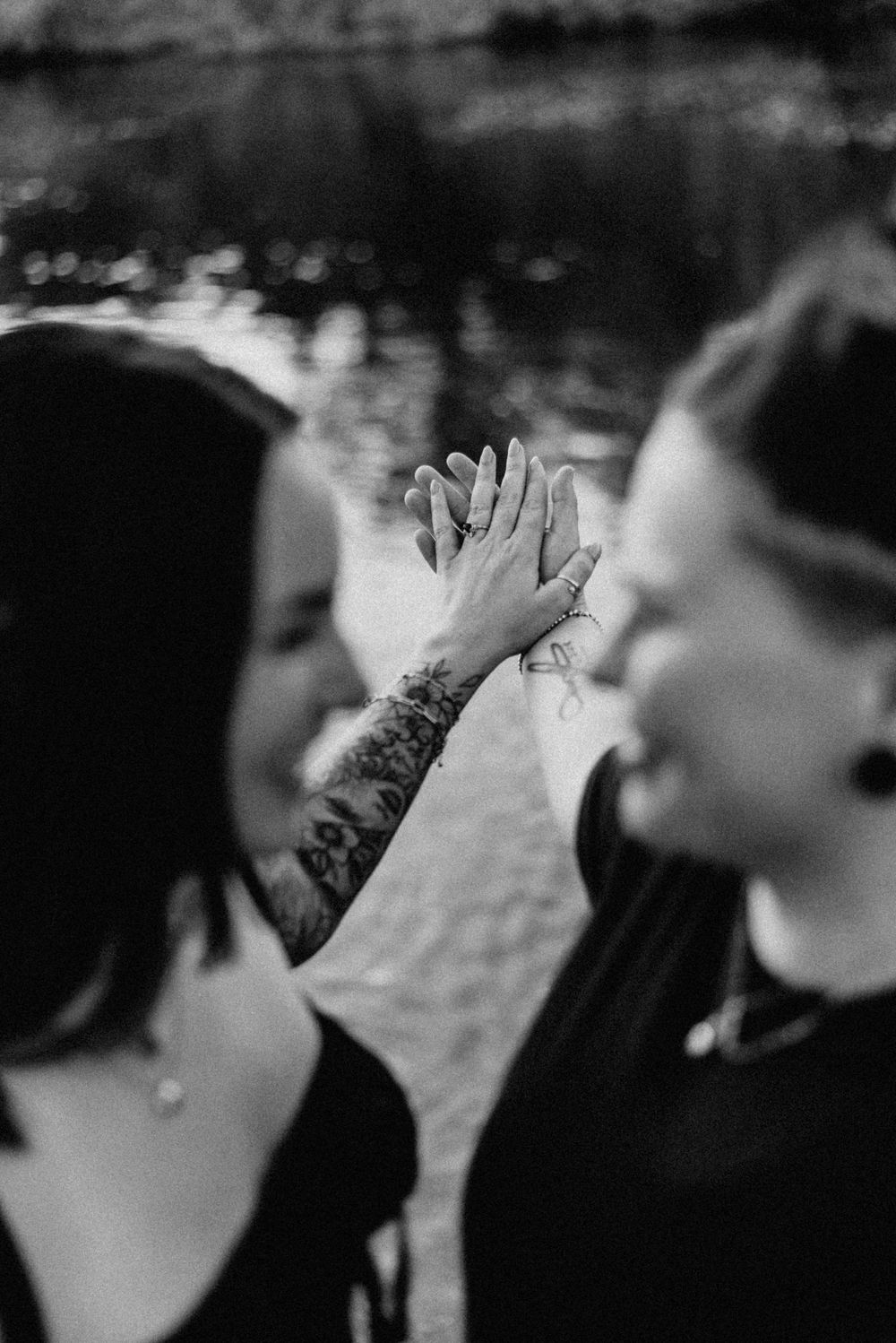 Black and white photo of tattooed hands clasped together in an intimate moment.