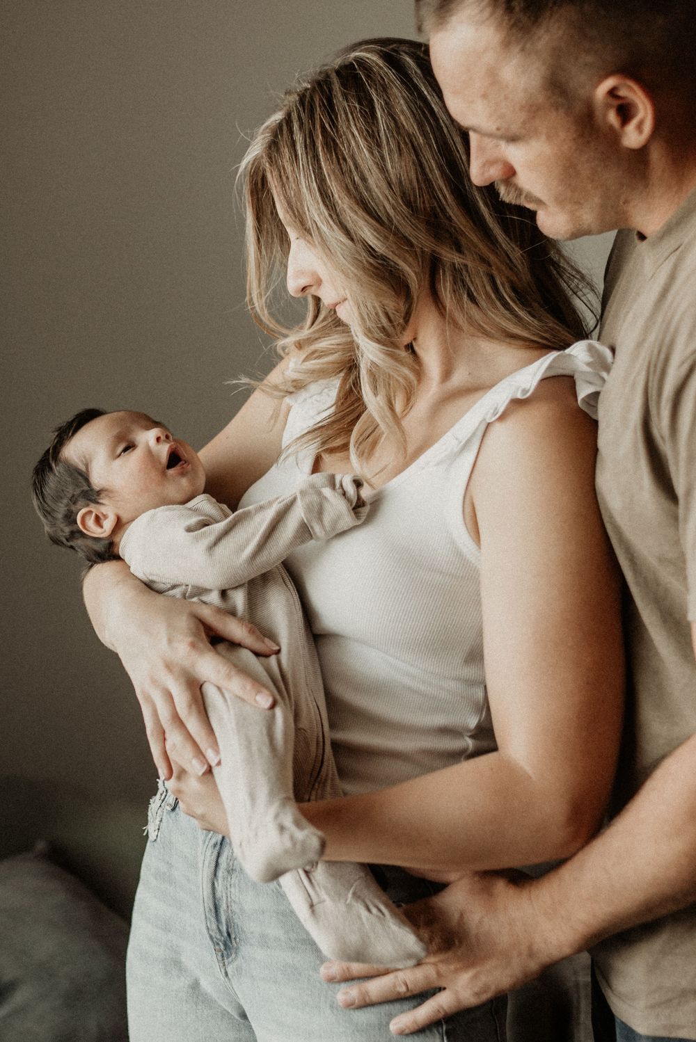 Intimate family portrait series showing tender moments with baby in neutral tones.