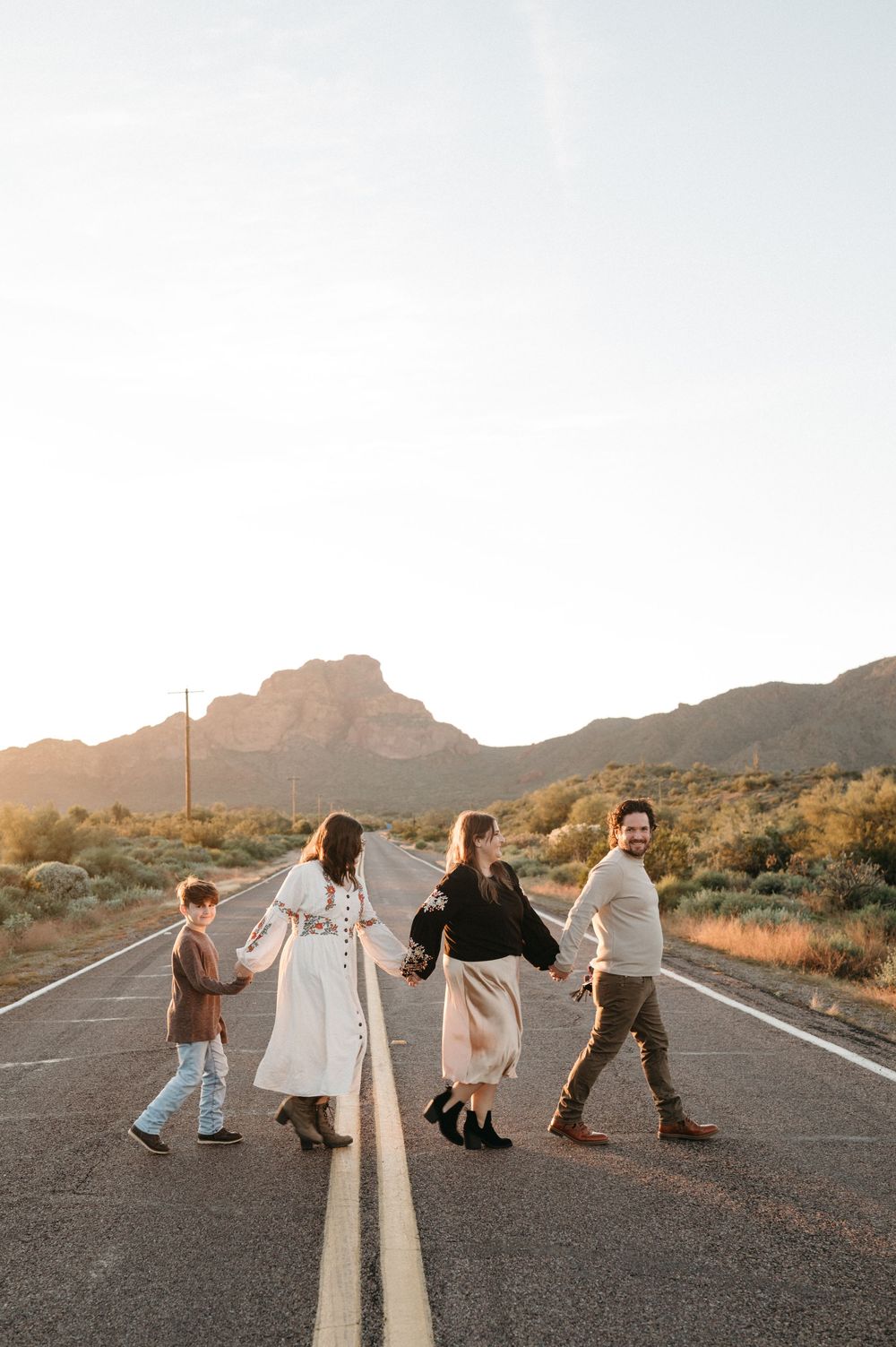 A sequence of four photos showing people playfully posing along a desert road at sunset with mountains in the background.