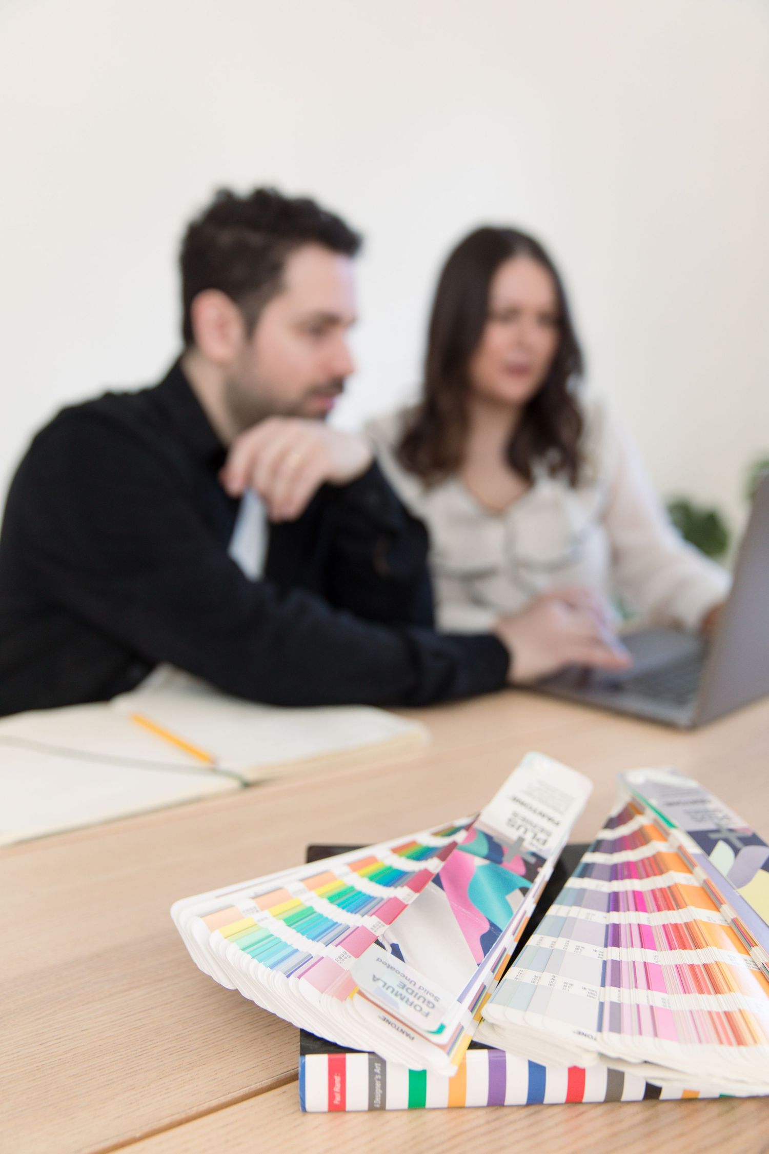 Color swatches and pantone cards spread on wooden table during creative meeting.