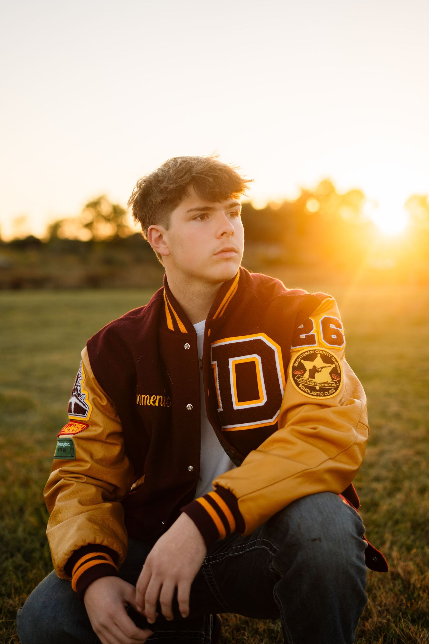 Senior portrait of student in varsity jacket during golden hour sunset.