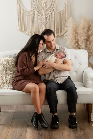 Modern family photoshoot on white couch with boho decor and pampas grass accents.