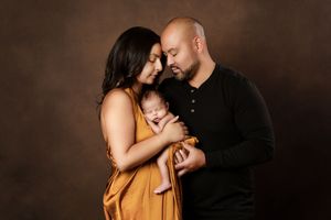 Intimate family portrait against dark brown background in studio setting.