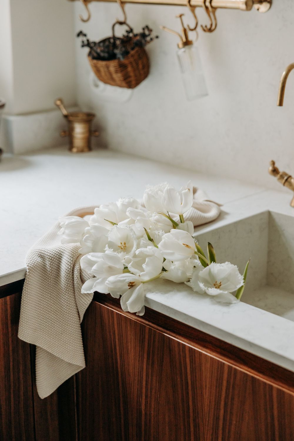 White tulips resting on a stone sink beside a linen towel in an elegant kitchen with brass fixtures.