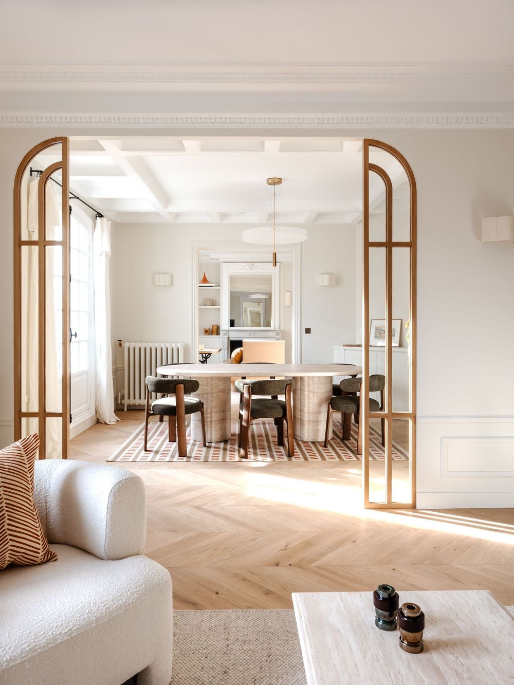 Elegant open-plan living and dining room with herringbone floors, arched doorway, white sofa, and neutral Scandinavian decor.