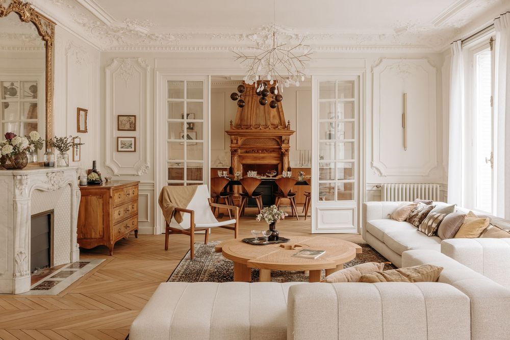 Elegant Parisian living room with white moldings, herringbone floors, marble fireplace, and classic French furniture.