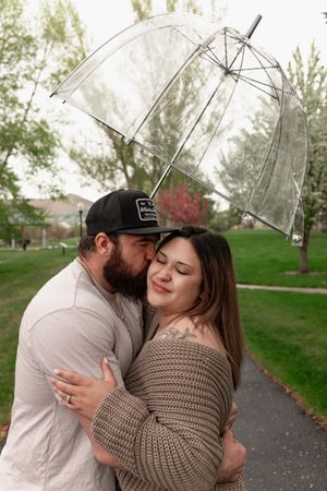 Couple embraces under clear umbrella on rainy spring day.