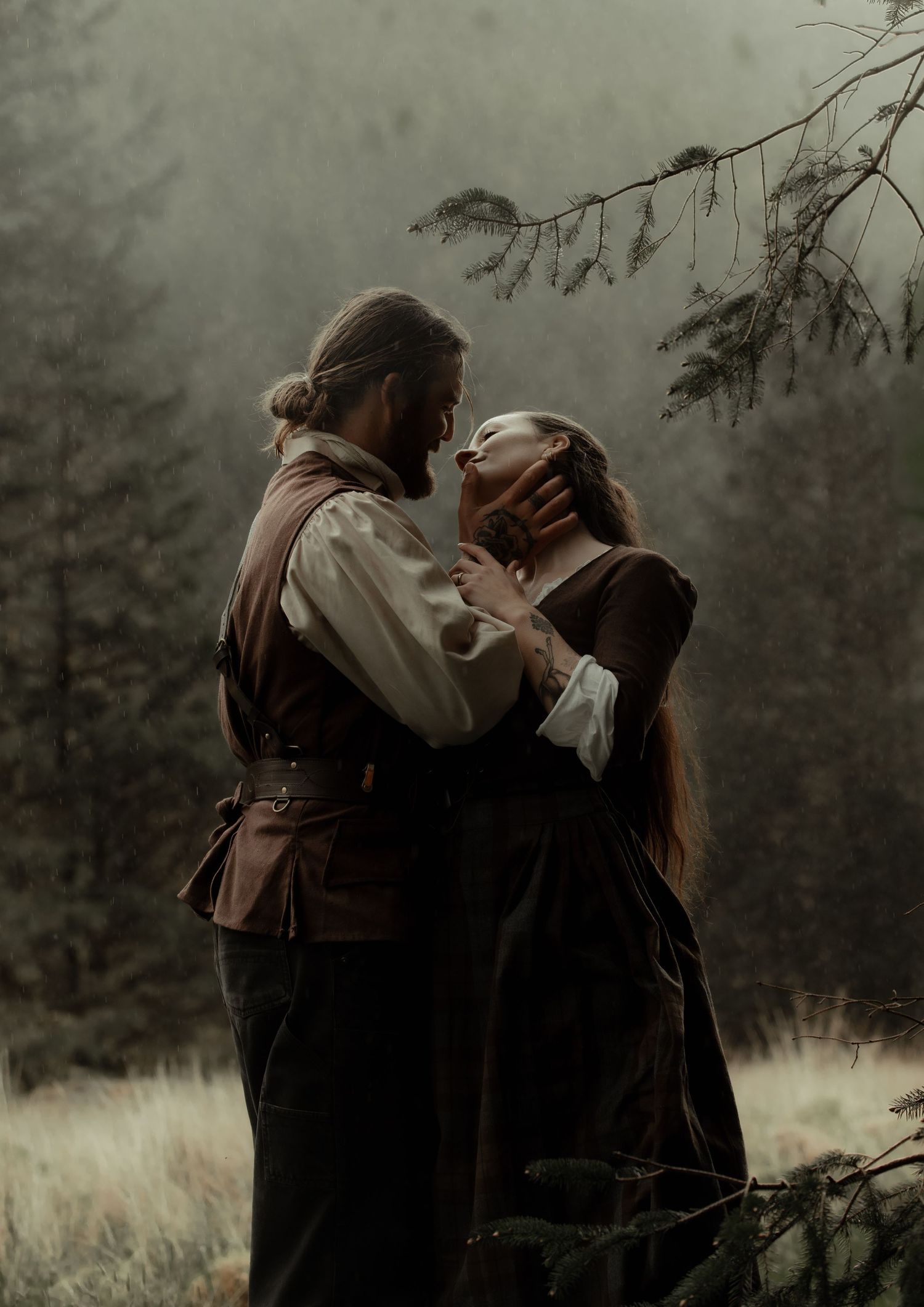 Dreamy, cinematic photo of a couple in medieval attire standing on a cliff, overlooking the water through a soft, hazy atmosphere.