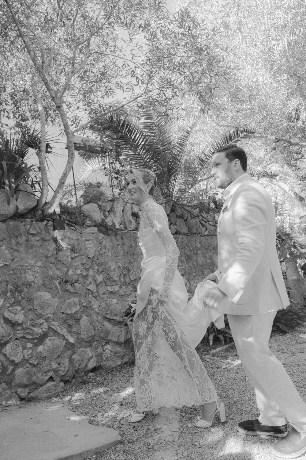 Black and white sequence showing figures in white protective suits inspecting a stone wall in a garden setting.