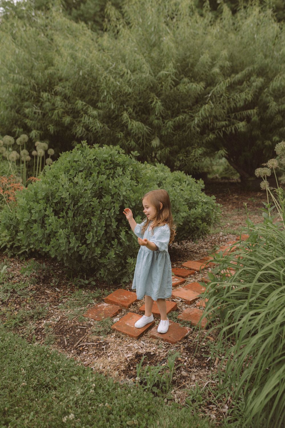 Small figure in blue dress explores garden pathway surrounded by lush greenery.