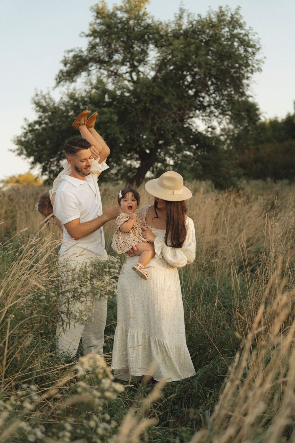 A family shares joyful moments together under a large tree at sunset.