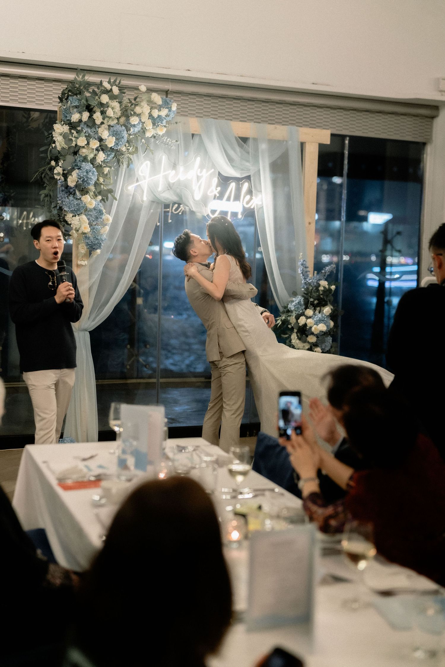 A couple shares their first kiss under a neon sign during their wedding reception.