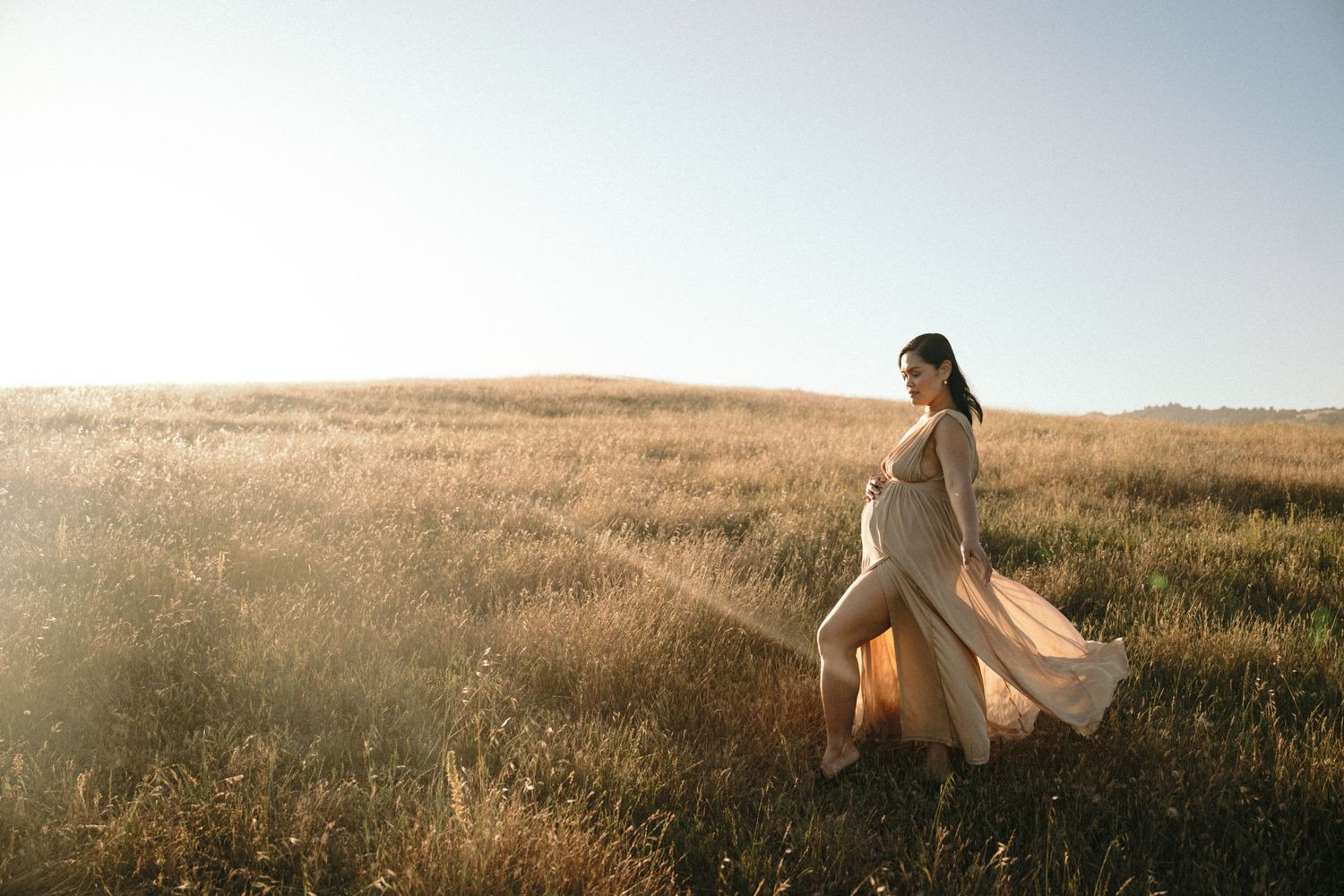 A person in a flowing white dress walks through a golden field at sunset creating a dreamy ethereal scene.