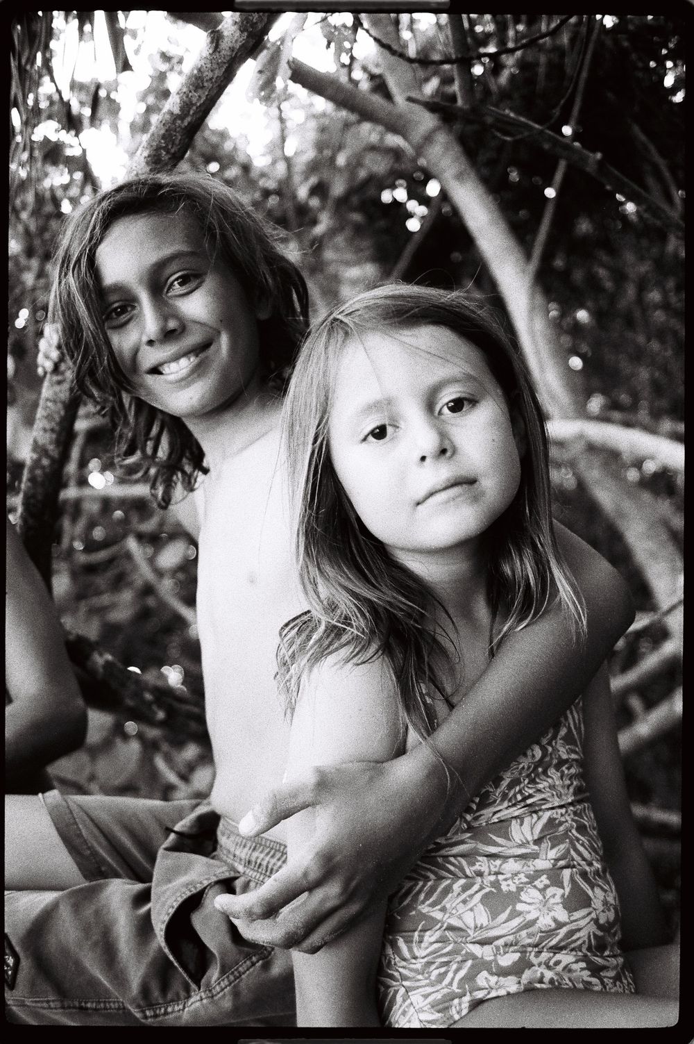 Black and white photo of two young children smiling outdoors among trees.