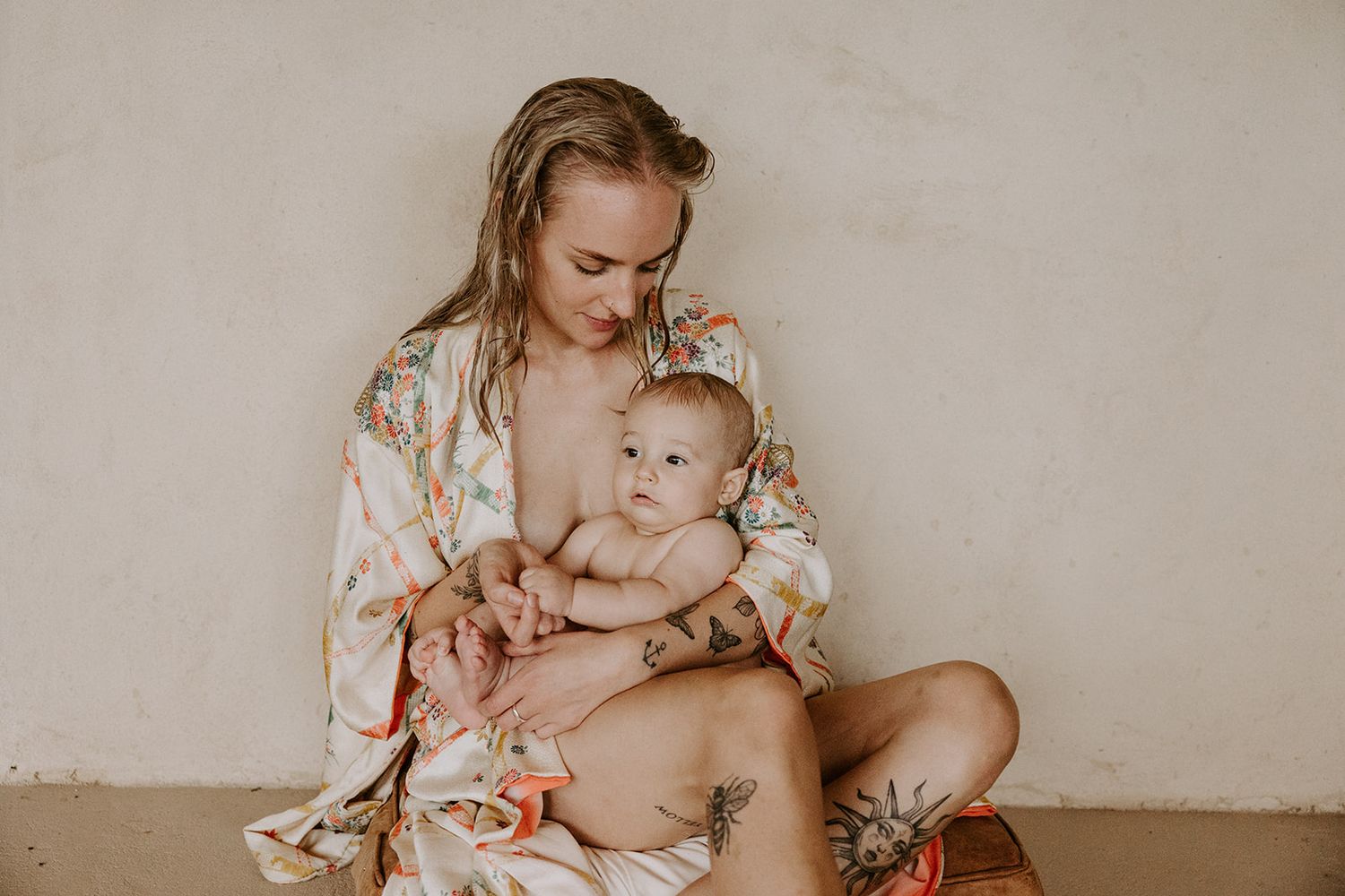 A parent in a floral dress holds and nurtures a baby in a series of intimate lifestyle portraits.
