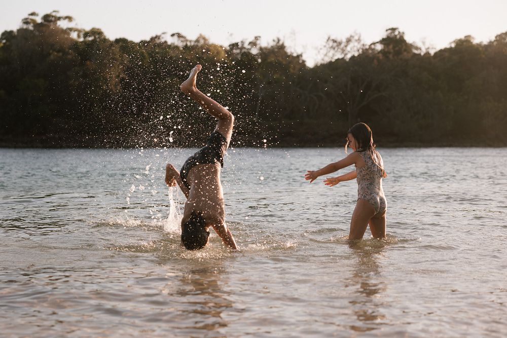 People splash and play in a lake during sunset creating ripples in the golden-lit water.